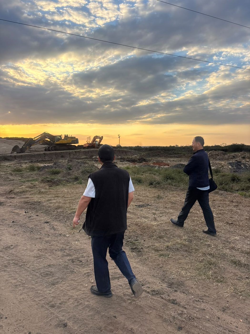 Supervisors inspecting bulk earthworks with excavators at sunset